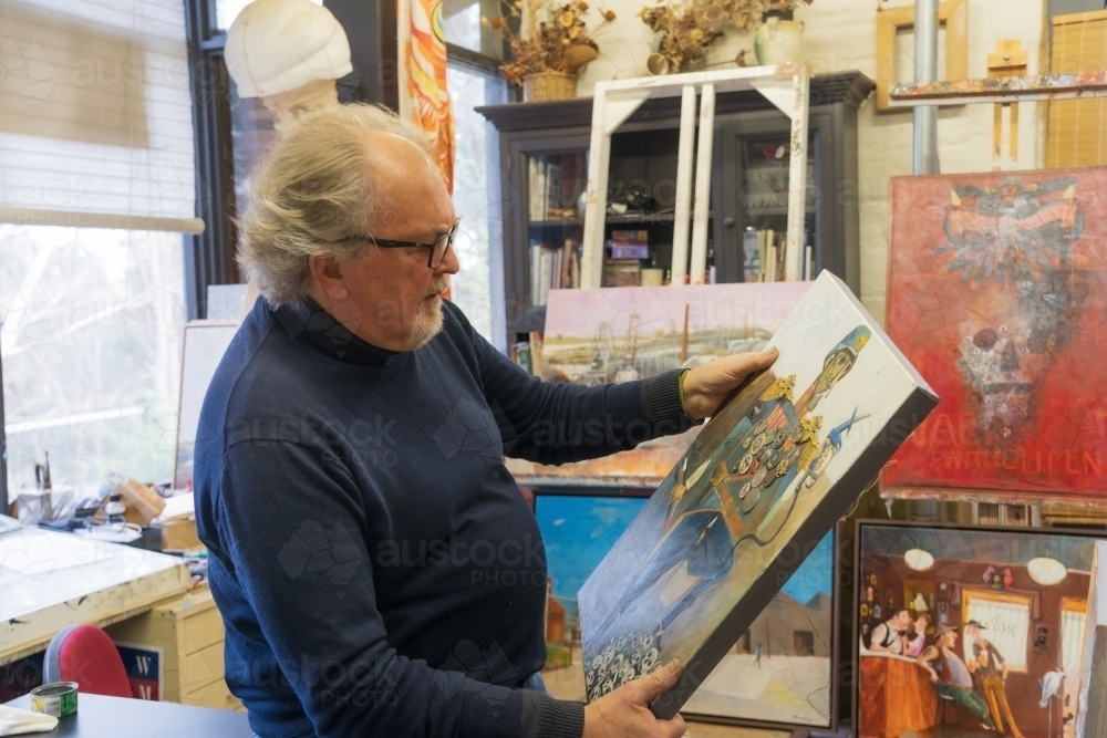 A distinguished male artist sitting admiring a painting in his studio - Australian Stock Image