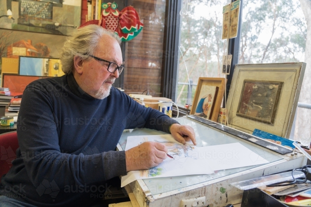 A distinguished male artist sketching on a desk in an art studio - Australian Stock Image