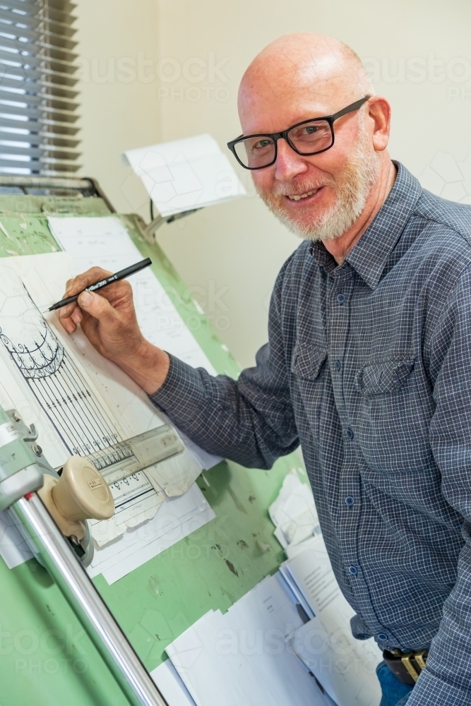 A draftsman wearing glasses sketching a design on a drawing board - Australian Stock Image