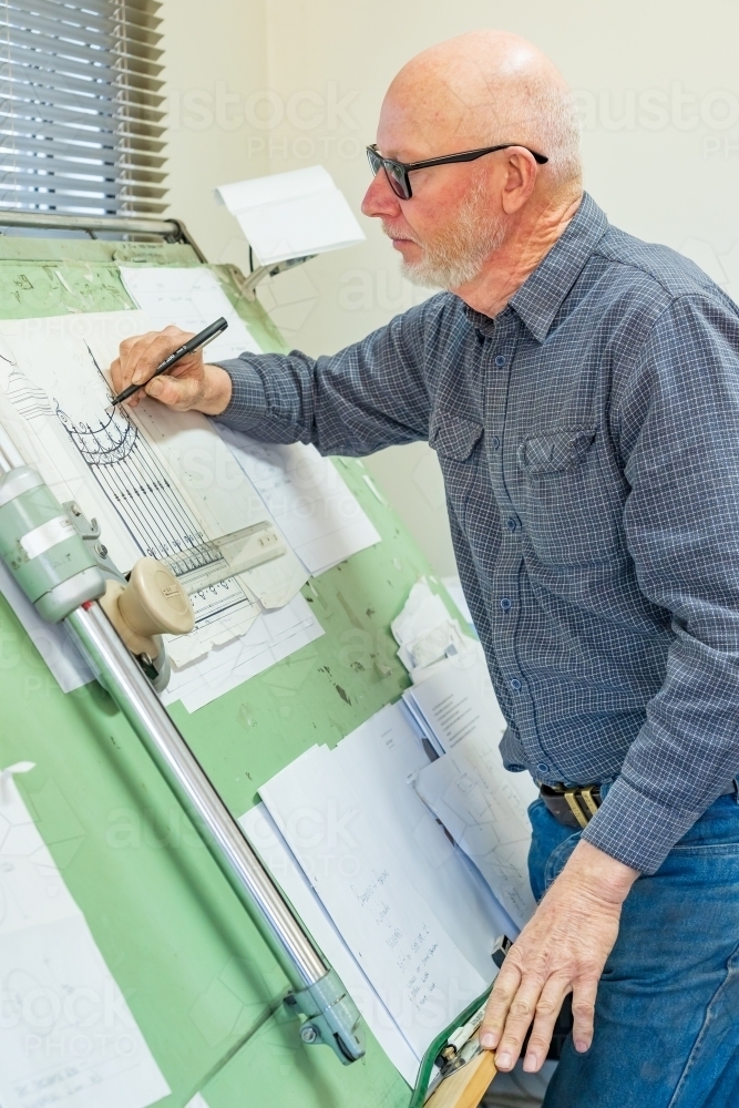 A draftsman wearing glasses sketching a design on a drawing board - Australian Stock Image