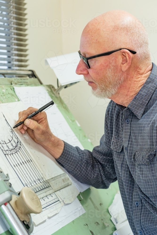 A draftsman wearing glasses sketching a design on a drawing board - Australian Stock Image