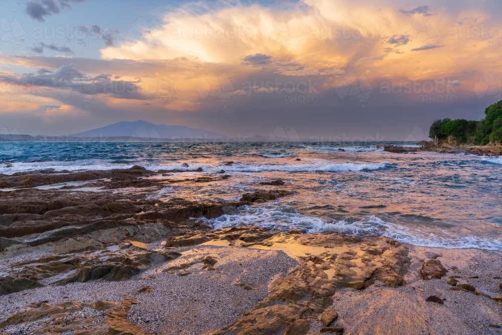A dramatic stormy sky over a rocky coastline in late afternoon light - Australian Stock Image