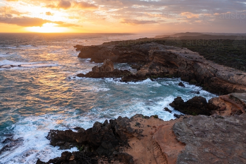 A dramatic sunset over waves crashing on a rugged coastline - Australian Stock Image