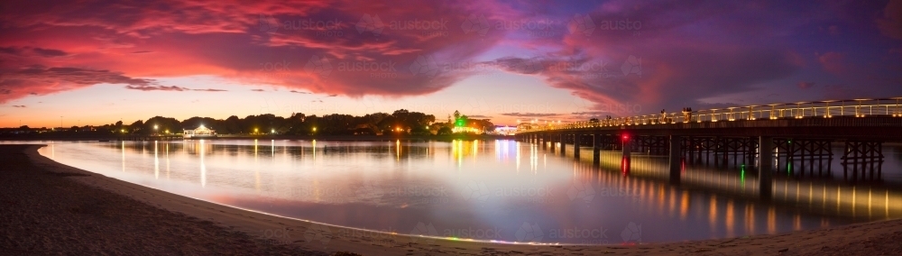 A dramatic sunset sky and bridges reflected in the still waters of a coastal river - Australian Stock Image