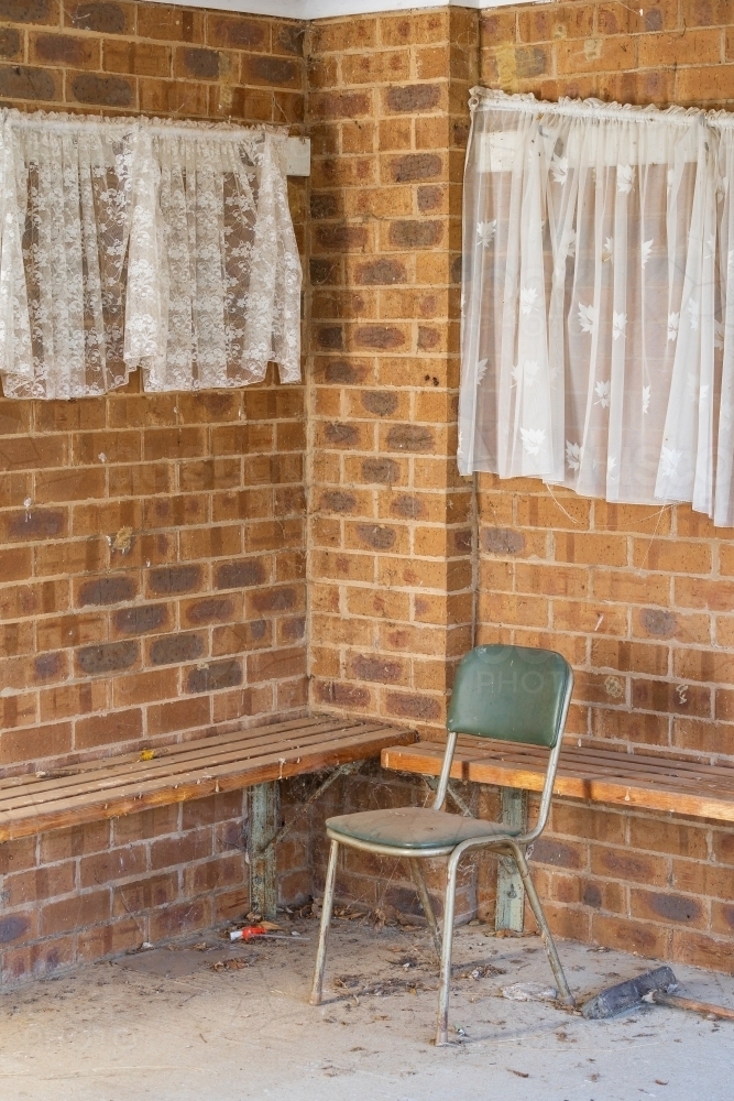 A dusty chair sitting in the corner of a brick room with lace curtains - Australian Stock Image