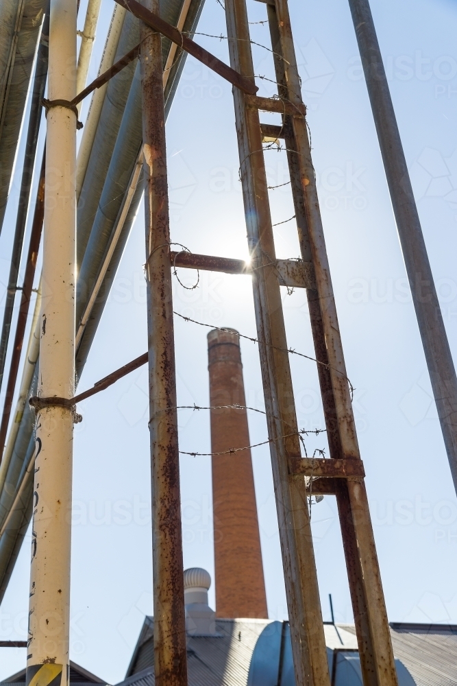 A factory chimney rising between a steel framework holding overhead pipes - Australian Stock Image