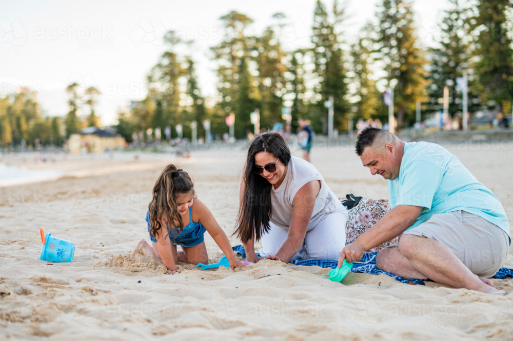 A family is playing in the sand by the beach as the sun sets in the background. - Australian Stock Image