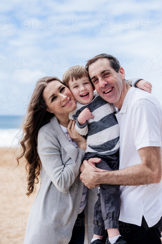 A family of a young boy, a male and a female smiling on a beach together - Australian Stock Image