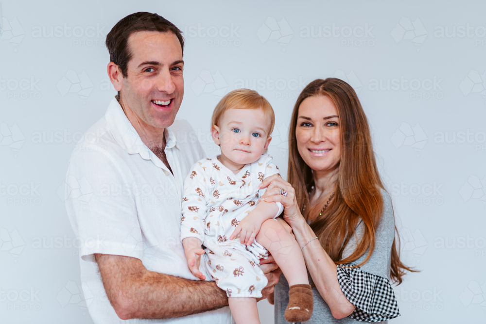 A family portrait of a mid-aged couple and their young boy, smiling against a white background - Australian Stock Image