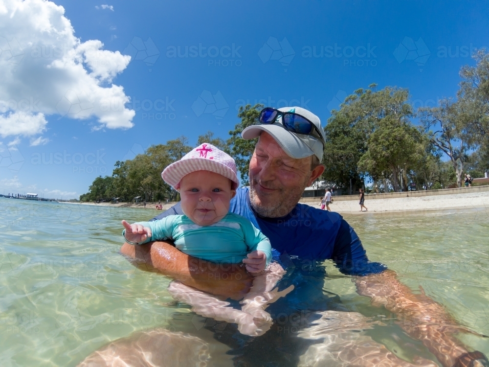A father and baby daughter playing in water at beach. - Australian Stock Image