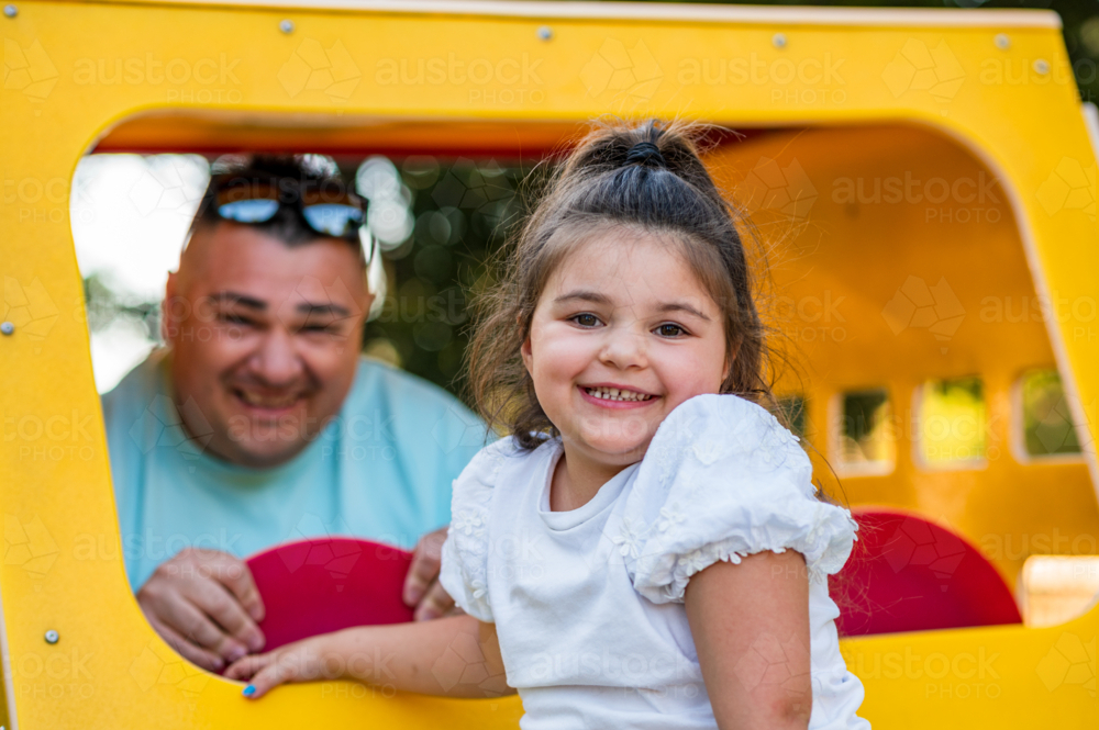 A father and his daughter enjoy their time at a yellow playhouse in the park during the afternoon - Australian Stock Image