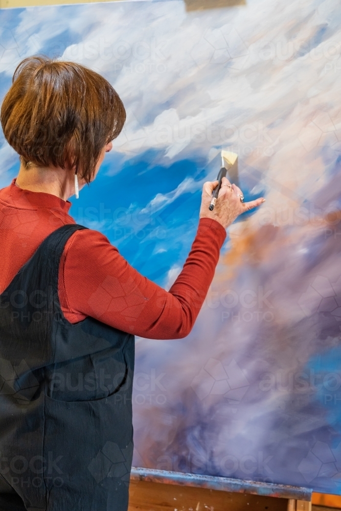 A female artist wearing overalls painting a large colourful canvas - Australian Stock Image