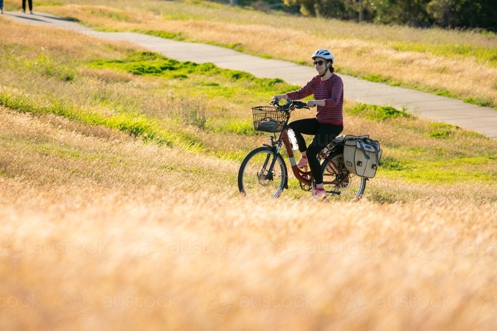 A female cyclist riding along a grassy lined bike path in Brisbane - Australian Stock Image