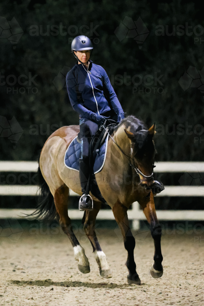A female practices on her horse in an arena at night - Australian Stock Image