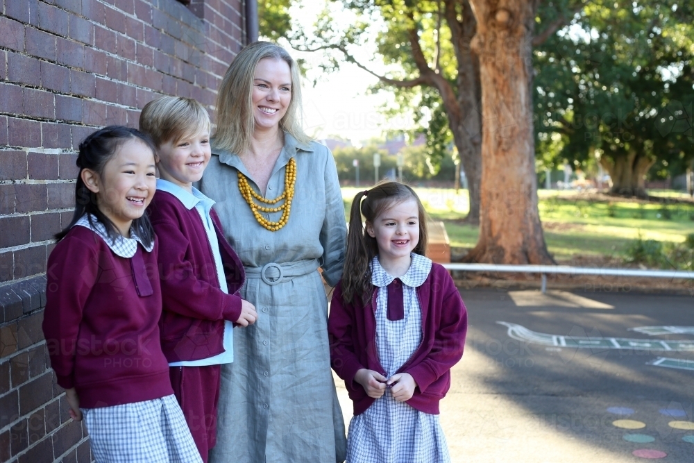 A female teacher and her students standing by the school building smiling - Australian Stock Image