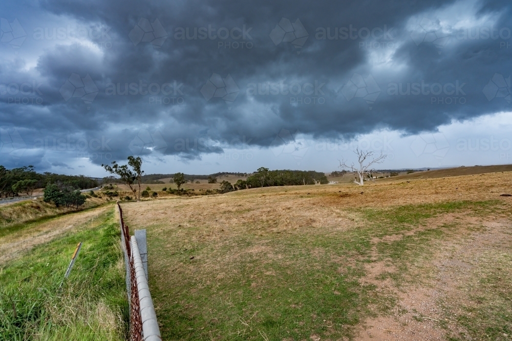 A fence line running over farmland under a dark storm front - Australian Stock Image