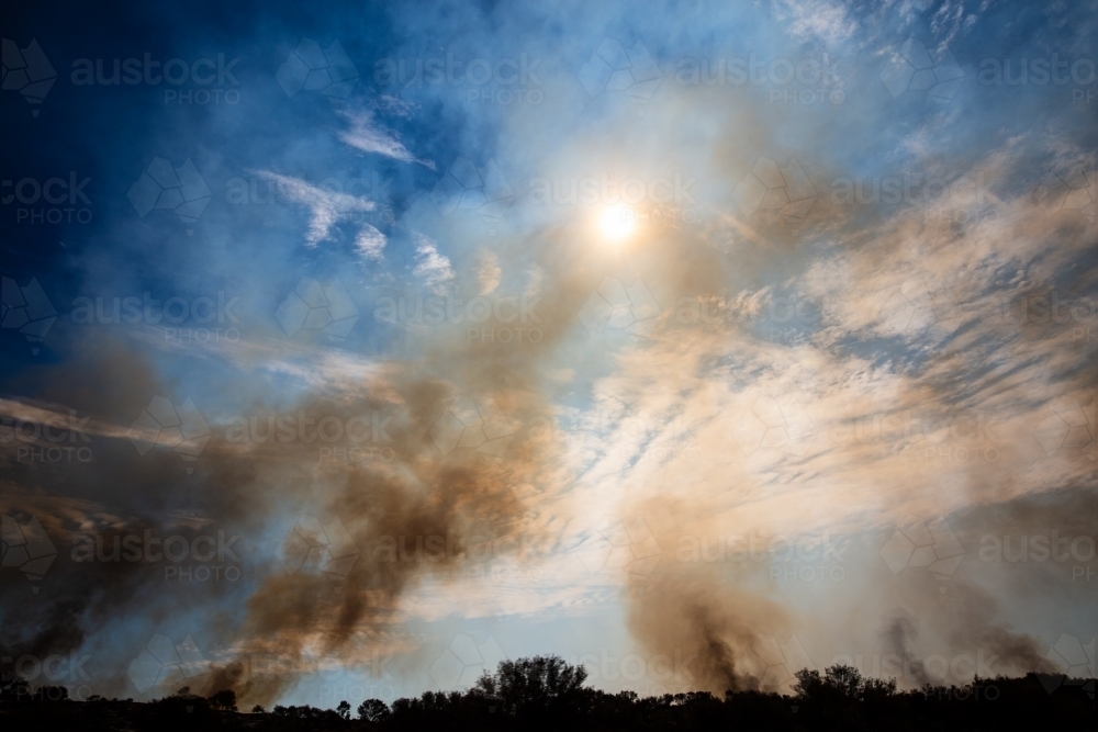 A few small fires making smoke in the sky caused by buring off. Central Australia. - Australian Stock Image