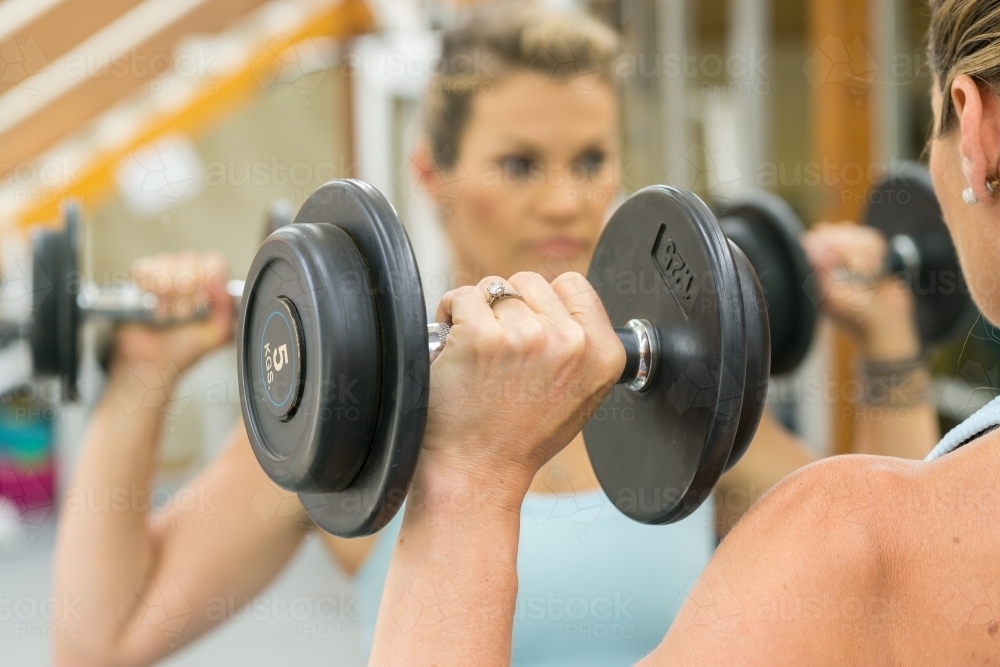 A fit woman lifting weights in front of a gym mirror - Australian Stock Image