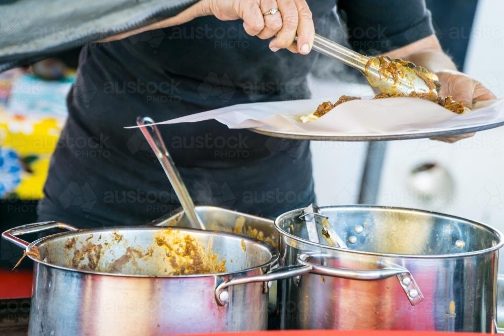 A food vendor using tongs to get food out of a saucepan - Australian Stock Image