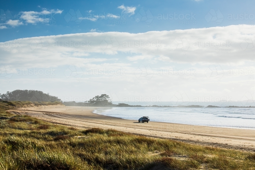 A four wheel drive vehicle drives along a deserted beach early in the morning. - Australian Stock Image