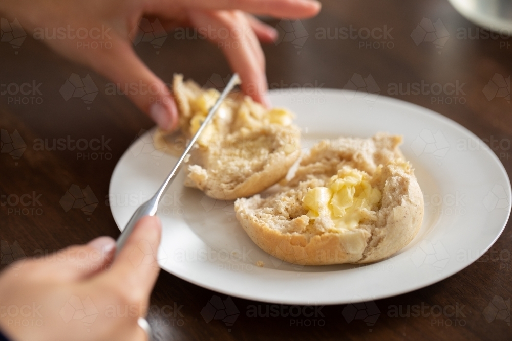 a fresh homemade bun being buttered with a knife - Australian Stock Image