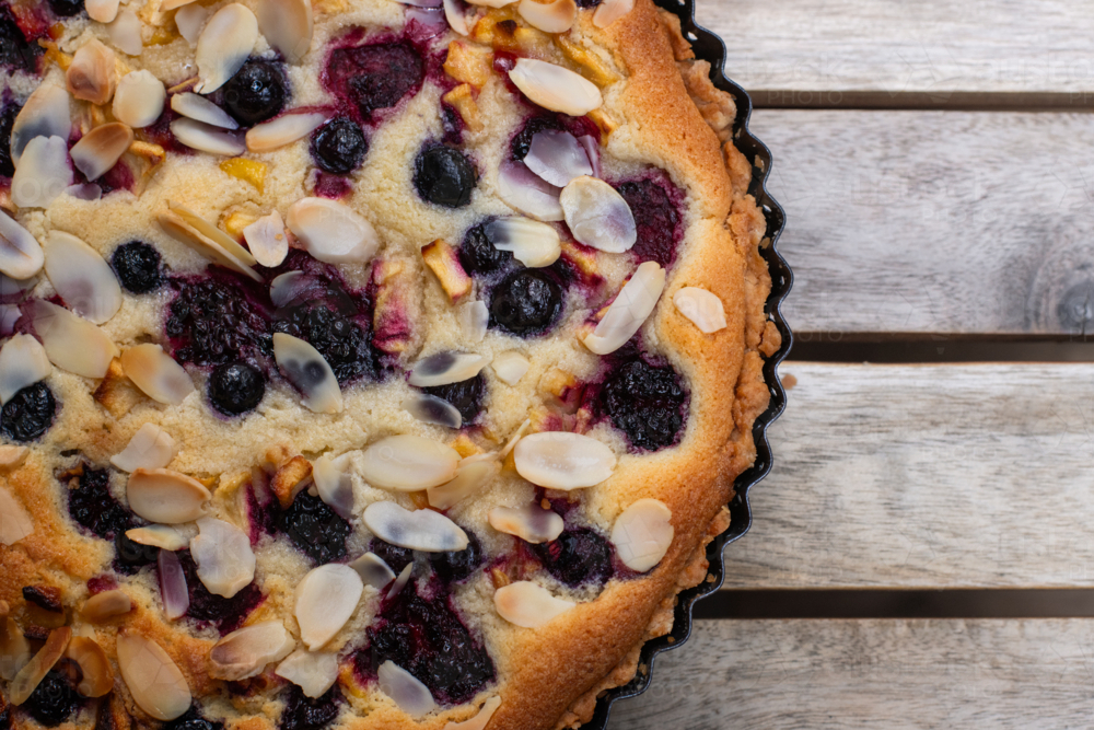 a freshly baked frangepane tart with berries and nuts, on a wooden table - Australian Stock Image
