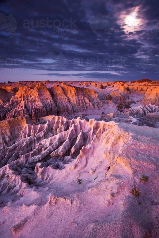 A full moon breaks through cloud above an eroded outback landscape at twilight - Australian Stock Image