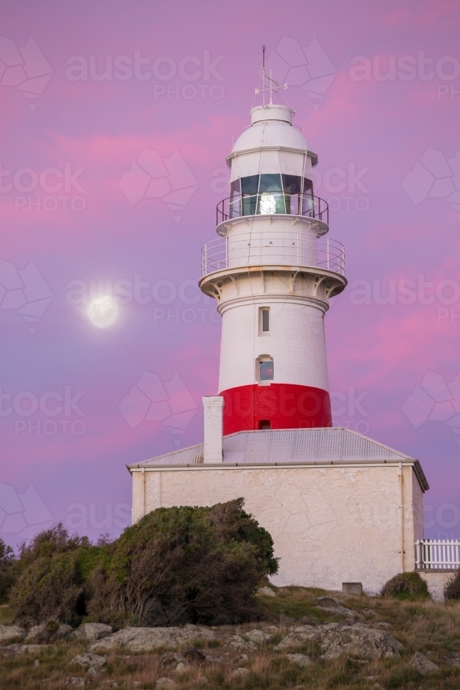 A full moon rising alongside a lighthouse at twilight - Australian Stock Image
