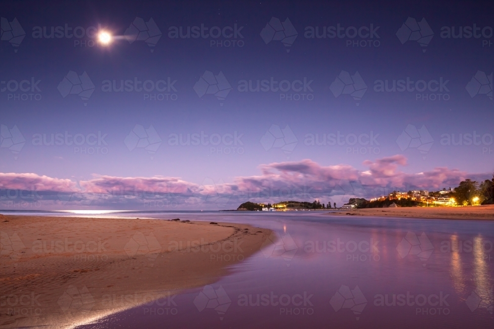 A full moon rising at twilight over a coastal lagoon - Australian Stock Image