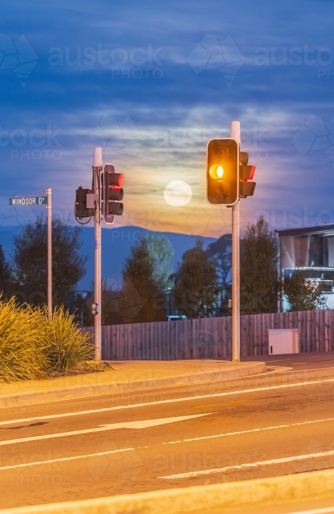 A full moon rising between traffic lights at an intersection - Australian Stock Image