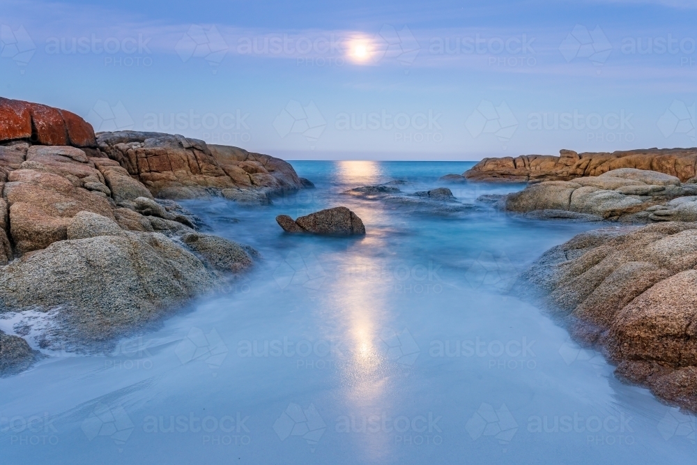 A full moon rising over an inlet along a rocky coastline - Australian Stock Image