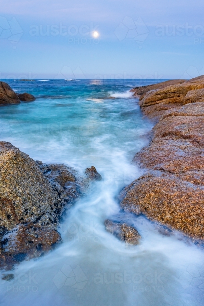 A full moon rising over an inlet along a rocky coastline - Australian Stock Image