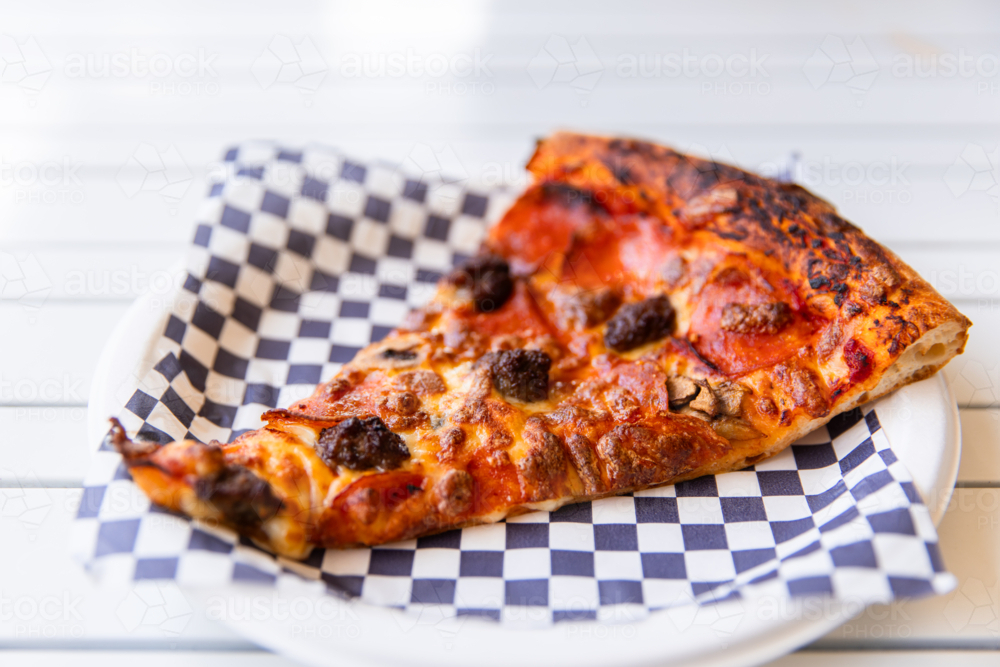 a generous slice of pizza on a paper plate - Australian Stock Image