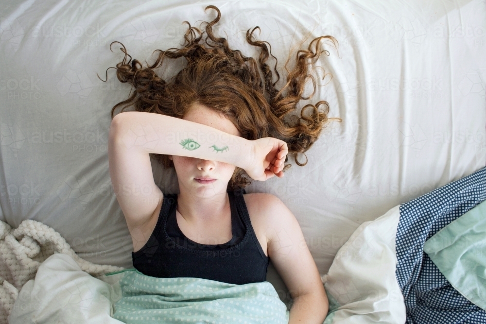 A girl laying in bed pretending to sleep from above - Australian Stock Image