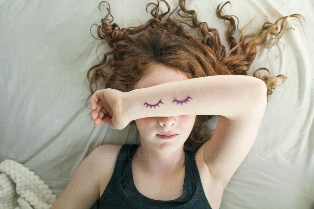 A girl laying in bed pretending to sleep from above - Australian Stock Image