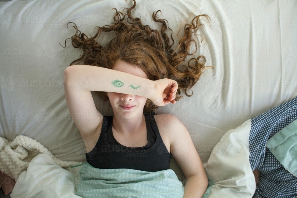 A girl laying in bed pretending to sleep from above - Australian Stock Image