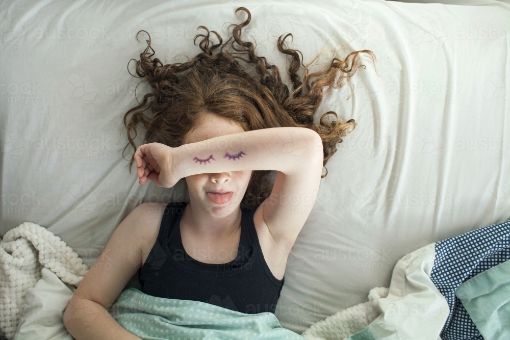 A girl laying in bed pretending to sleep from above - Australian Stock Image