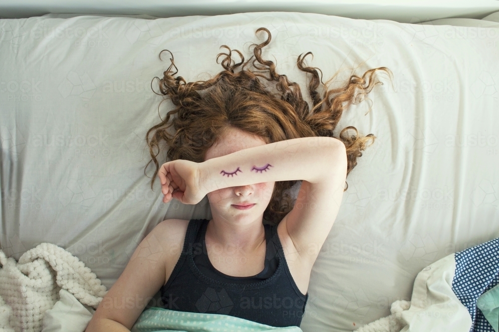 A girl laying in bed pretending to sleep from above - Australian Stock Image