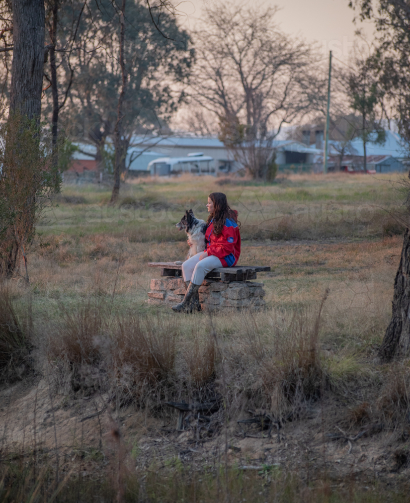 A girl sitting on a bench with her dog in a field - Australian Stock Image