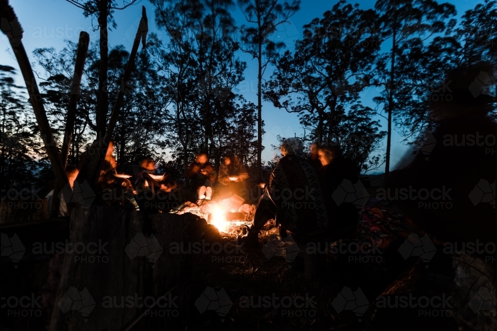 A group of people sitting around a campfire at night relaxing - Australian Stock Image
