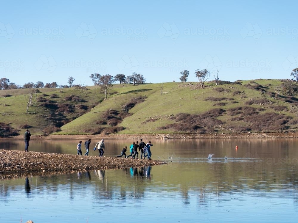 A group of people skimming stones over the water of a storage dam - Australian Stock Image