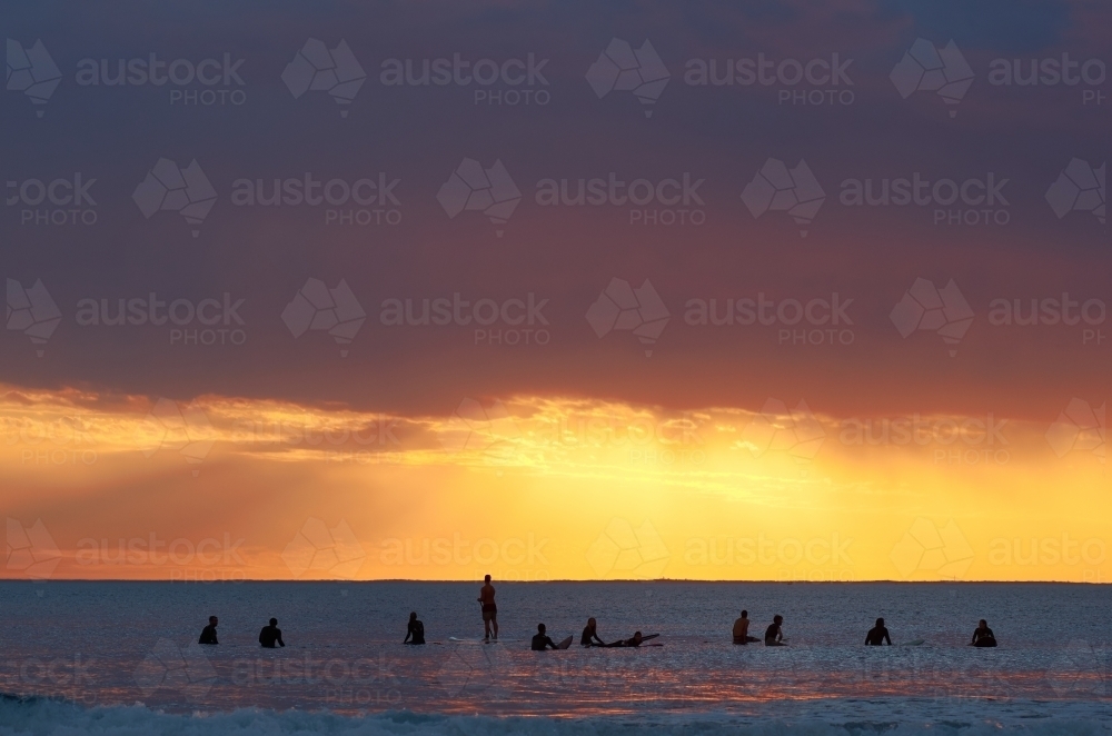 A group of surfers waiting for the next wave, as the sun sets in the background - Australian Stock Image