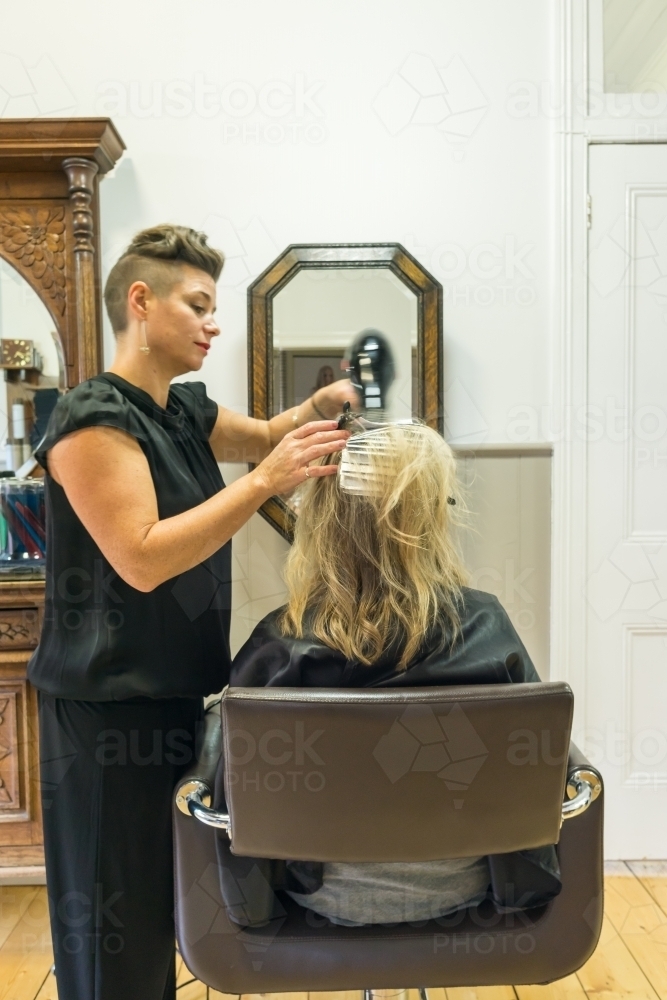 A hair dresser blow drying a ladies hair in a salon - Australian Stock Image