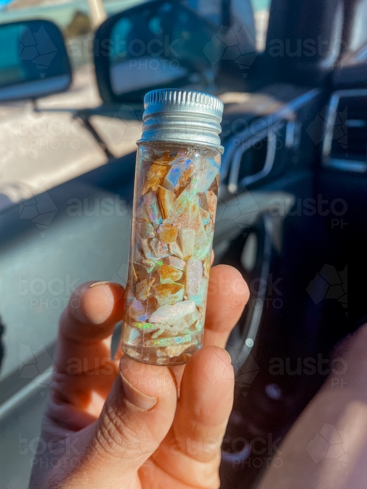 A hand holding a small glass vial of opal shards - Australian Stock Image