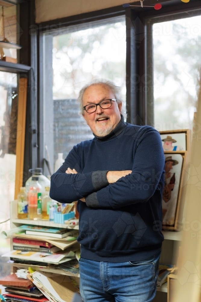 A happy male artist standing with folded arms in his studio - Australian Stock Image