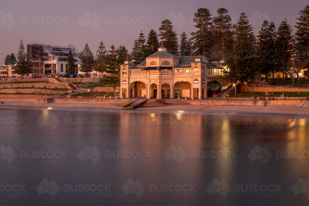 A heritage beachside pavilion glowing at dusk reflected in calm water framed by Norfolk pines - Australian Stock Image