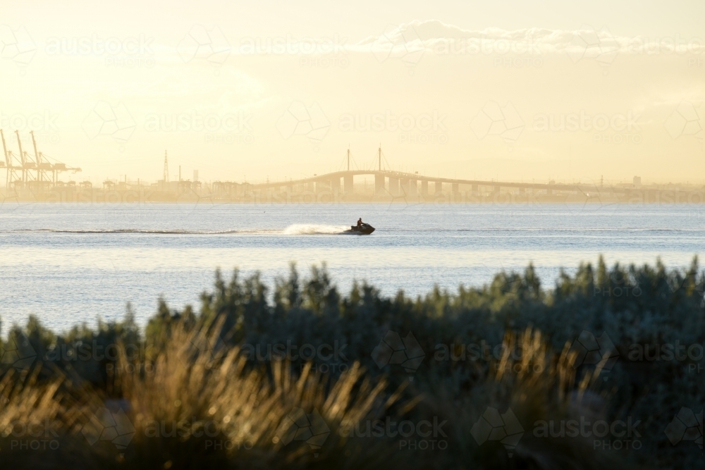 A jet ski rider speeding across Port Phillip Bay with the West Gate Bridge in the background - Australian Stock Image