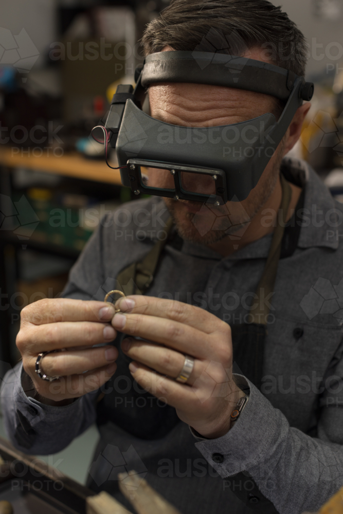 A jeweller wearing goggles and focusing on a ring in his hands - Australian Stock Image