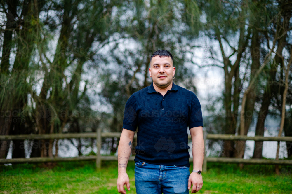 A man in his thirties stands in a tranquil park setting surrounded by trees and water - Australian Stock Image