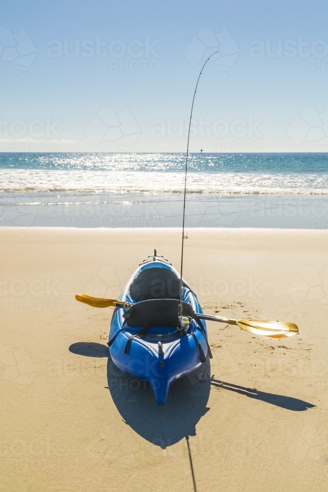 A kayak sitting on a beach with a paddle and fishing rod on board - Australian Stock Image